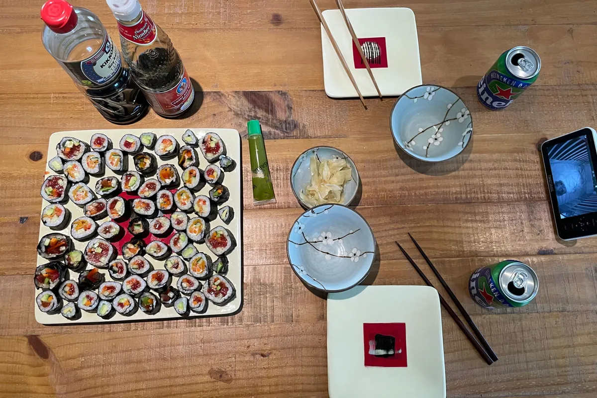 Table filled with a vegan sushi plate, some plates, drinks and a baby monitor