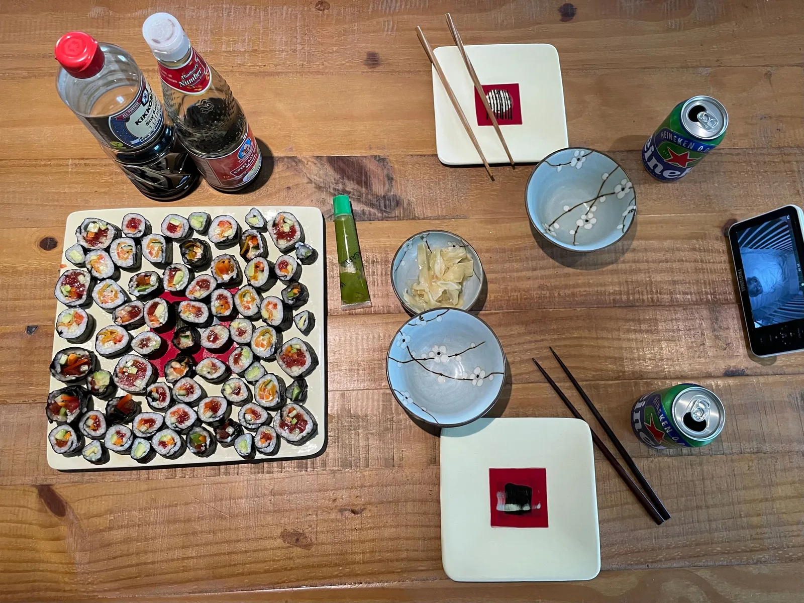 Table filled with a vegan sushi plate, some plates, drinks and a baby monitor